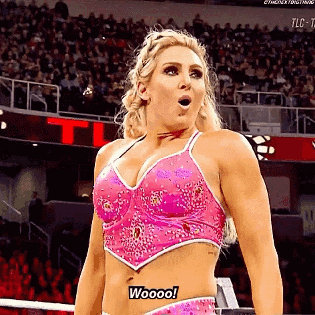 a woman in a pink top is standing in a wrestling ring and saying woooo .