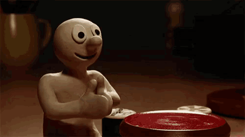 a cartoon character is giving a thumbs up while sitting at a table next to a bowl of food .