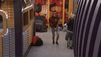 a man in a red shirt is walking down a hallway while a woman stands behind him .