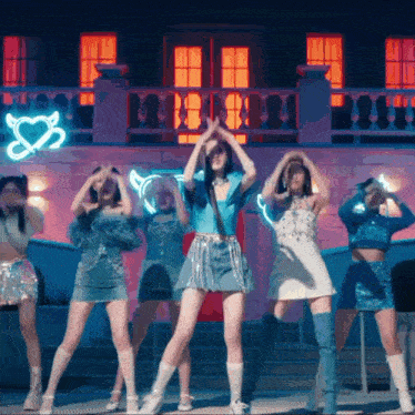 a group of women are dancing in front of a building with a neon sign that says s2 on it