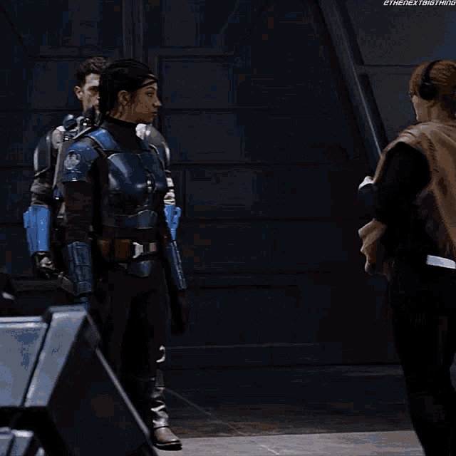 a woman wearing headphones talks to a woman in a blue armored outfit