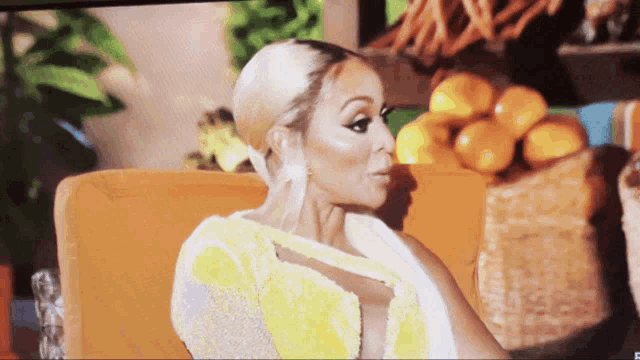 a woman in a yellow top sits on a couch with oranges in the background