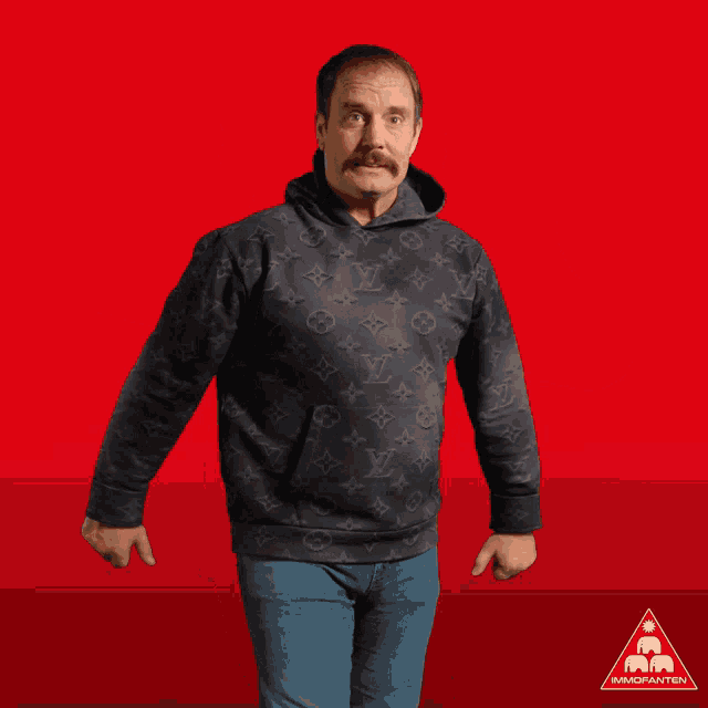 a man in a black louis vuitton hoodie gives two thumbs up in front of a red background