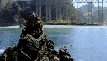 a bridge over a body of water with a large rock in front of it