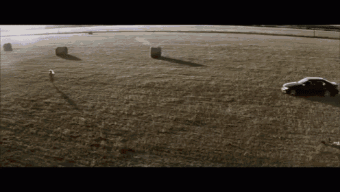 a car is driving through a field with bales of hay
