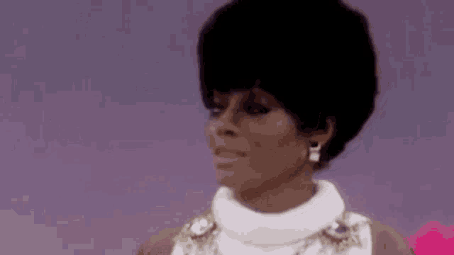 a close up of a woman 's face with a purple background . she is wearing a white dress and earrings .