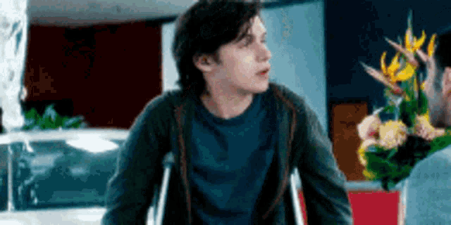 a man in crutches is talking to another man holding flowers .