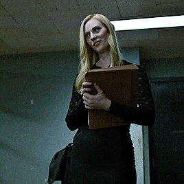 a woman in a black dress is holding a folder and smiling