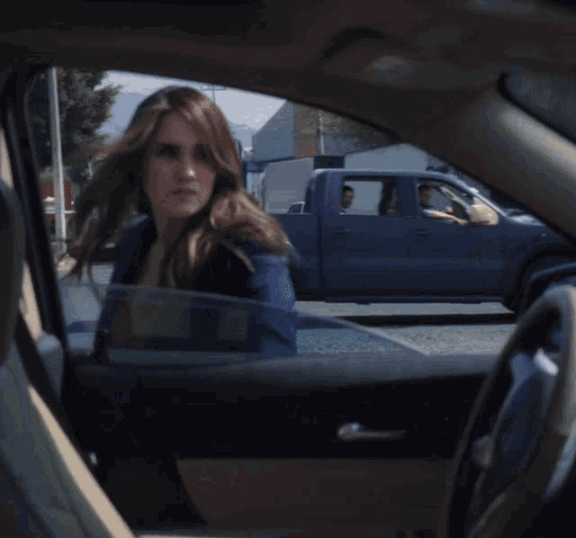 a woman is sitting in a car with a van parked behind her