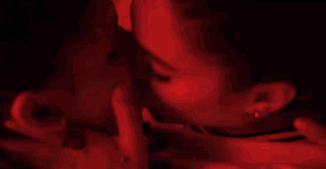 a man and a woman are kissing in a dark room with red lights .