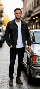 a man wearing a black denim jacket is standing in front of a silver car
