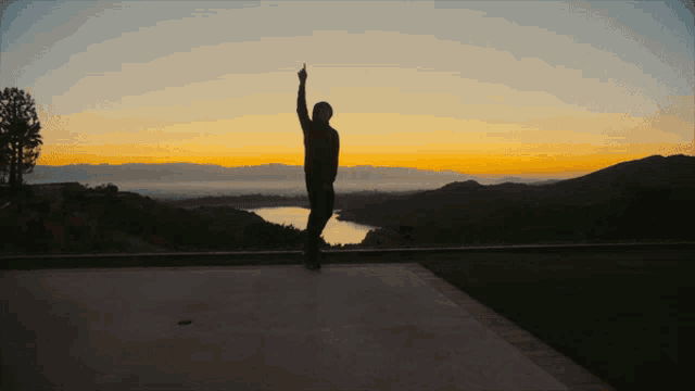 a man stands in front of a sunset with his hand up