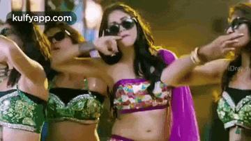 a group of women are dancing together and one of them is wearing sunglasses and a purple top .