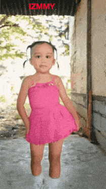 a little girl in a pink dress stands in front of a sign that says izmmy on it