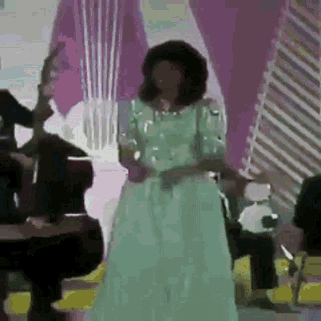 a woman in a green dress is singing into a microphone while standing in front of a piano .
