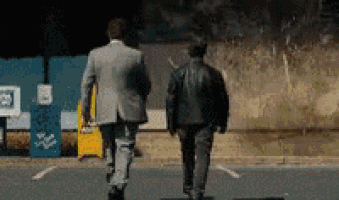 two men in suits are walking down a street in a parking lot .