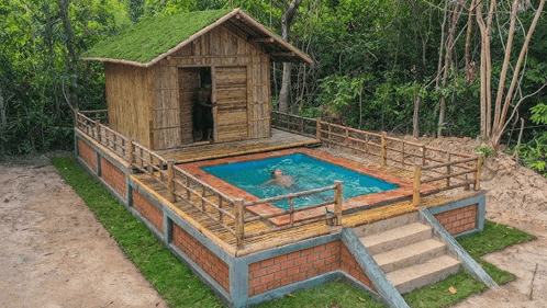 a man is swimming in a small pool in front of a small hut