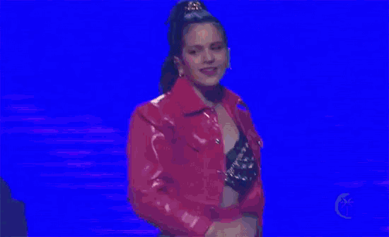 a woman is wearing a red jacket and a black bra while standing on a stage .