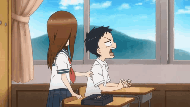 a boy and a girl are sitting at desks in a classroom and the girl is putting her hand on the boy 's back