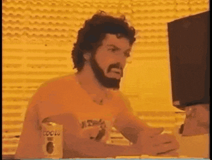 a man with a beard is sitting at a desk in front of a computer screen .