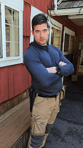 a man with his arms crossed standing in front of a red building