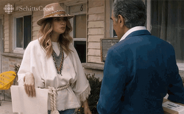 a woman in a hat is talking to a man in a suit with #schitts creek on the bottom right