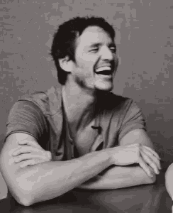 a man is sitting at a table with his arms crossed laughing .