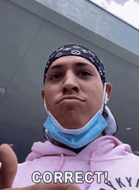 a man wearing a bandana and a face mask is giving a thumbs up sign .