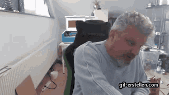 a man is sitting in a chair with the website gif-erstellen.com visible