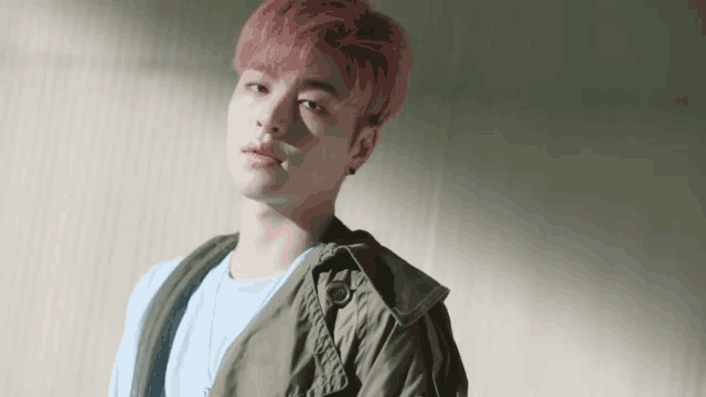 a young man with pink hair and a blue shirt is standing in front of a wall .