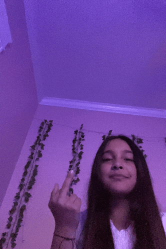 a girl is giving the middle finger in front of a purple wall