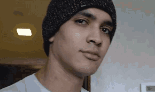 a man wearing a black beanie and a white shirt looks at the camera