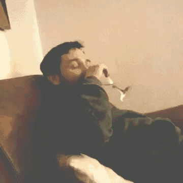 a man laying on a couch drinking from a glass
