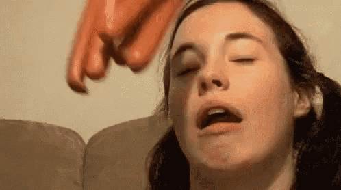a woman is sitting on a couch with her eyes closed while a bunch of hot dogs are flying in the background .