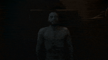 a close up of a shirtless man with a beard making a funny face in the dark .
