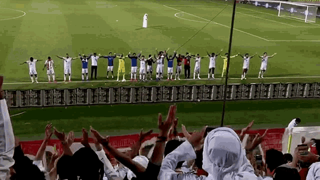 a group of people are standing on a soccer field with their arms in the air