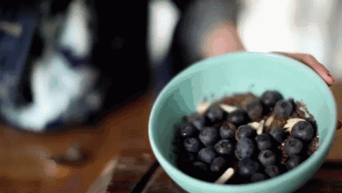 a person is holding a bowl of blueberries on a wooden table