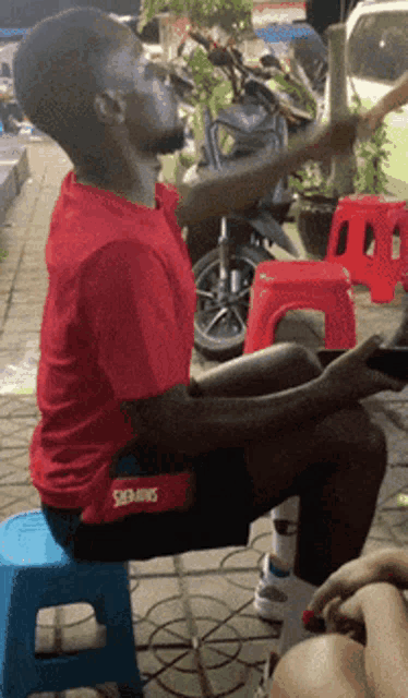 a man sitting on a blue stool wearing a red shirt that says skins
