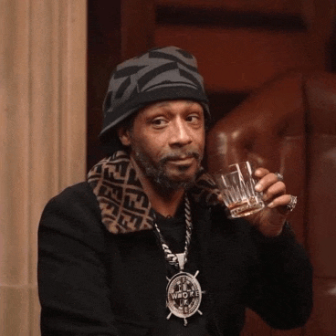 a man wearing a hat and a pendant that says i 'm who i am drinking a glass of whiskey
