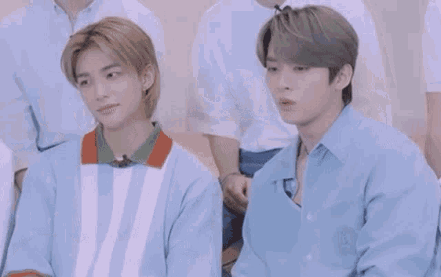 two young men are sitting next to each other with their arms crossed in a room .