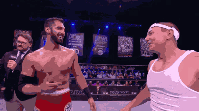 a wrestler in a white tank top stands next to another wrestler