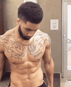 a shirtless man with a beard and tattoos on his chest and shoulder is standing in a gym .