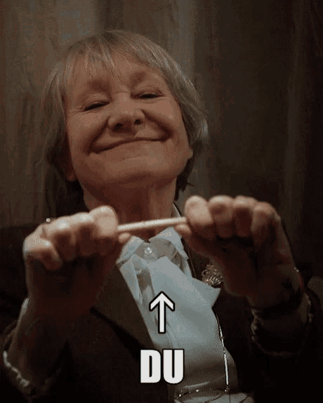 an older woman is smiling and holding a cigarette with an arrow pointing up and the word du underneath