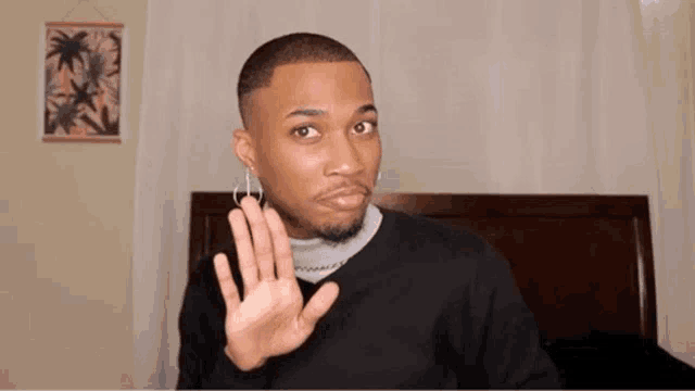 a man wearing hoop earrings and a black sweater is making a stop gesture with his hand .