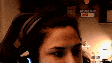 a woman wearing headphones looks at the camera with a stream sign in the background