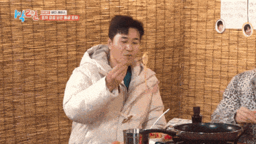 a man in a white jacket is eating noodles with a frying pan in front of him with the number 2 on it