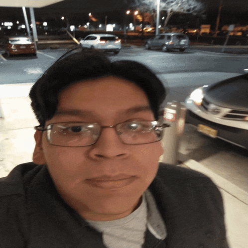 a man wearing glasses is standing in a parking lot with cars