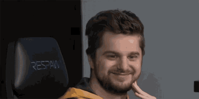 a man with a beard is sitting in a chair with his hand on his face and smiling .