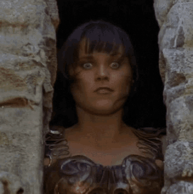 a woman is peeking out of a stone wall and making a surprised face