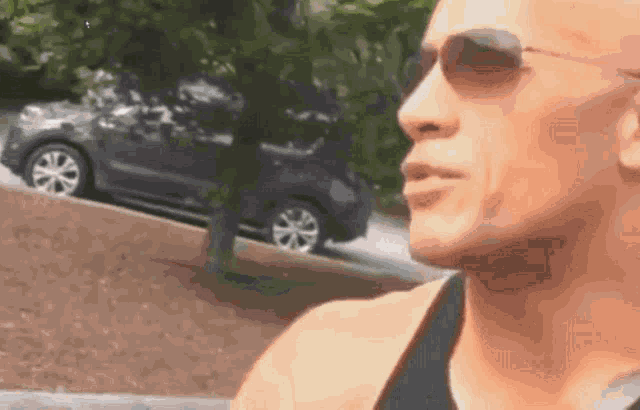a man wearing sunglasses is looking at a car that is going down a hill